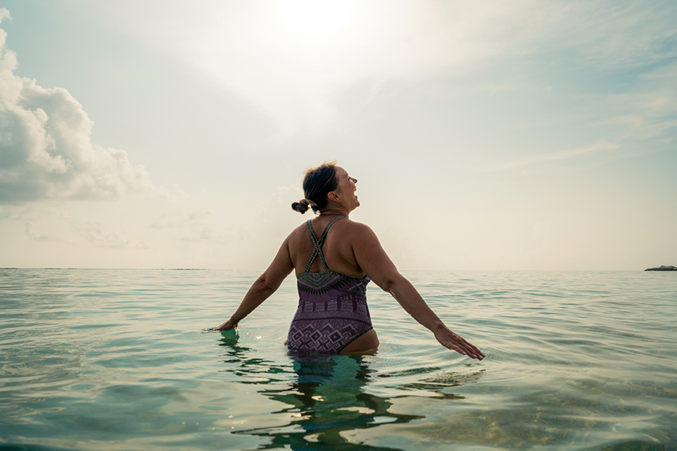 A woman standing in the sea, she is looking up at the sky and laughing
