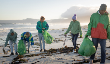 A group of five people are on the beach, cleaning up rubbish