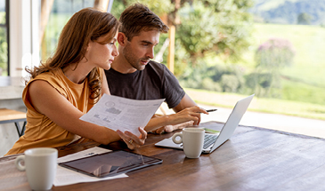 A young couple sitting at a table in their home, they are reviewing documents and looking at a laptop