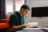 A boy in a green hoodie sitting at his desk reading a book